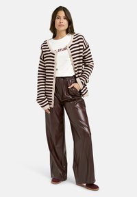 Gestreifte Cardigan in Dunkelbraun und Creme, oversized Passform, kombiniert mit hoch-taillierten, glänzenden bordeauxfarbenen Kunstlederhosen und bordeauxfarbenen Schuhen.