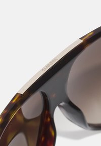 Skildpaddemønster solbriller med en slank sort ramme, brune gradientlinser og en metallic guld accent på stangen med "CARRERA" indgravering.