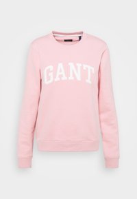 Sweat-shirt rose en tissu doux, avec un col rond, des manches longues, et un grand lettrage blanc "GANT" sur le devant.