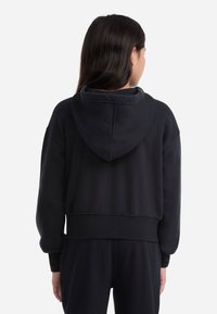 Sudadera negra corta con capucha y cordón. Hecha de un tejido suave, presenta puños y dobladillo acanalados, textura lisa y costuras mínimas.