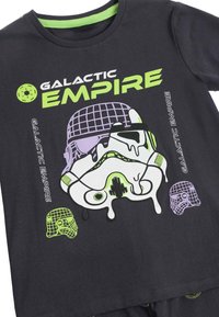Camiseta negra con un gráfico en verde neón y púrpura de un casco de ciencia ficción derritiéndose y el texto "Imperio Galáctico" en fuentes en negrita y contorneadas.