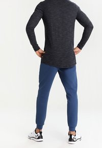 Mörkgrå långärmad topp med en strukturerad yta, i kombination med blå smala sweatpants och svart-vita träningsskor.