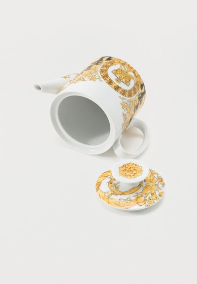 Λευκό πορσελάνινο τσαγιέρα με περίτεχνα κίτρινα και χρυσά λουλουδένια και σπειροειδή μοτίβα, εμφανιζόμενο με ανοιχτό καπάκι που ακουμπάει δίπλα του σε λευκή επιφάνεια.