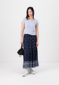 Top justo azul claro, saia maxi azul marinho com bordado floral branco, bolsa preta e ténis brancos. Tecido suave com design em camadas.