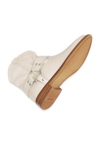 Botín de cuero blanco con punta redonda y tacón de madera bajo. Presenta una correa con anillo de metal y herrajes decorativos en plata. Suela plana.