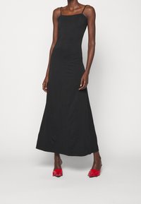 Czarna, bezrękawnikowa sukienka maxi z kwadratowym dekoltem, dopasowanym gorsetem i zwiewnym dołem. Połączona z czerwonymi sandałami na obcasie.