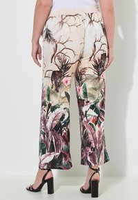 Pantaloni in tessuto chiaro e morbido, con un vivace motivo tropicale, caratterizzati da modelli di leopardo e vari disegni di fogliame verde e rosa.