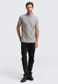 Grå polo-shirt med krave og korte ærmer, parret med sorte bukser og sorte sko. Skjorten har et lille logo på brystet.