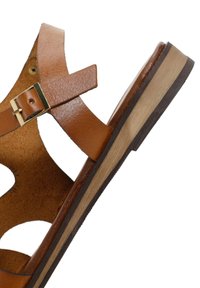 Tan leren sandaal met open ontwerp, met kruislings gespen, goudkleurige gesp en een gelaagde houten zool met zwarte accenten.