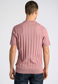 Sweter z krótkim rękawem, dzianinowy, w kolorze pyłowego różu, z okrągłym dekoltem i dopasowanym krojem, w zestawieniu z ciemnymi dżinsami o gładkiej fakturze.