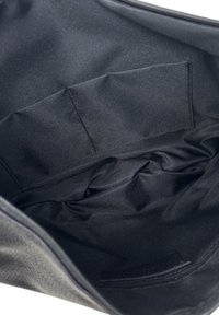 Černá tkanina uvnitř tašky, ukazující prošívanou obdélníkovou kapsu a zip podél horní hrany.