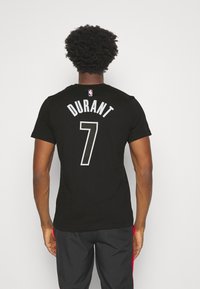 Černé tričko s krátkým rukávem s nápisem "DURANT" a číslem "7" v bílém písmu na zadní straně, s etiketou NBA na límci.