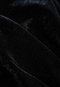 Čierny zamatový materiál s hladkou, mäkkou textúrou, ktorý má jemný lesk a mäkký záves. Záhyby vytvárajú na látke jemné vlny.