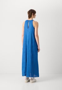 Blå linnmaxiklänning med ett nyckelhål i ryggen, med en lös passform och en slät textur. Bärs med vita sneakers och ljusgrå strumpor.