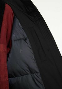 Svart jacka med en vadderad innerfoder, med en något glänsande yta. Det inre tyget är mörkt med ett subtilt mönster.