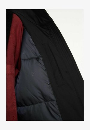 Schwarze Jacke mit einer gesteppten Innenausstattung, die eine leicht glänzende Textur aufweist. Der Innenstoff ist dunkel mit einem subtilen Muster.