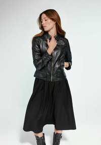 Czarna skórzana kurtka z zamkiem błyskawicznym, dopasowany kształt i pikowany materiał. W połączeniu z czarną, szeroką spódnicą do kolan i czarnymi botkami na obcasie.