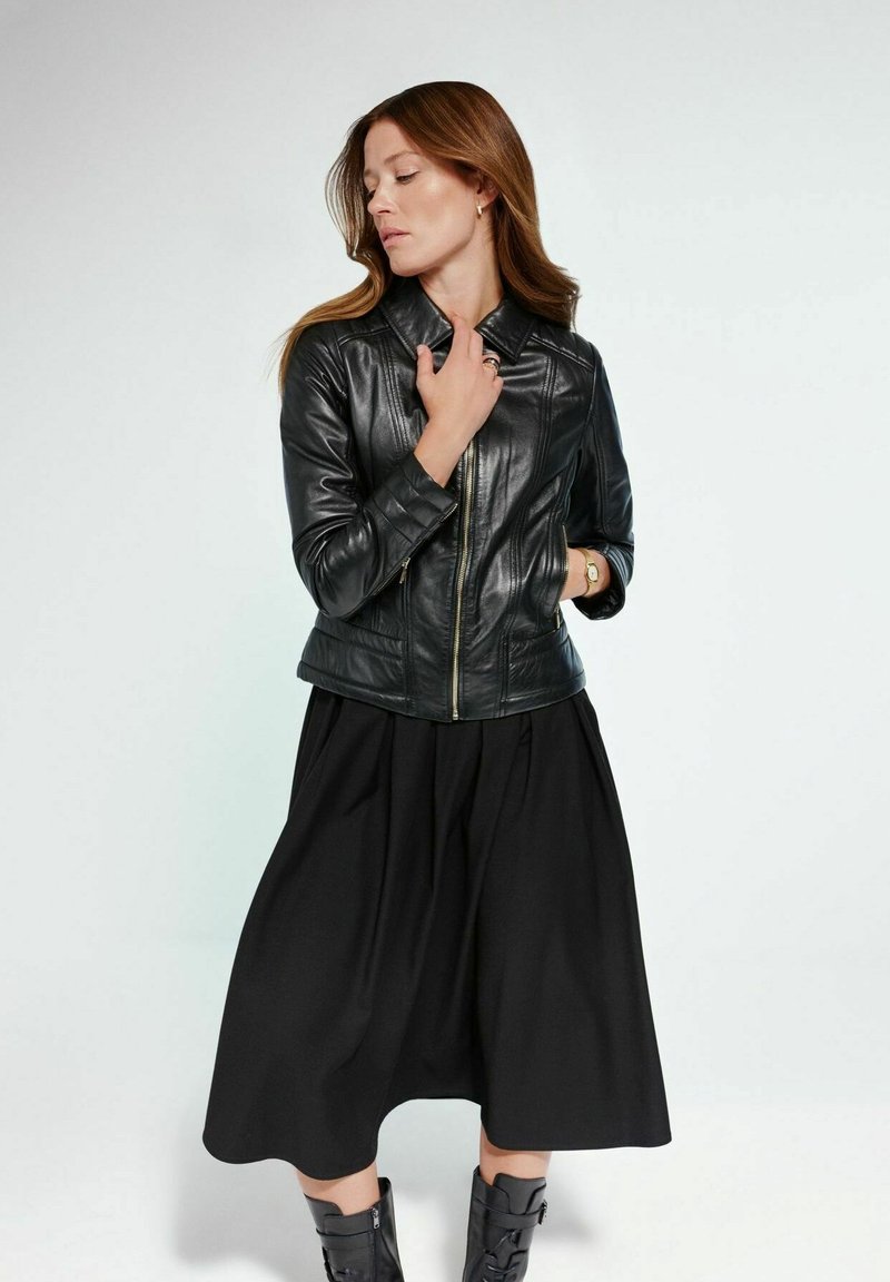 Czarna skórzana kurtka z zamkiem błyskawicznym, dopasowany kształt i pikowany materiał. W połączeniu z czarną, szeroką spódnicą do kolan i czarnymi botkami na obcasie.