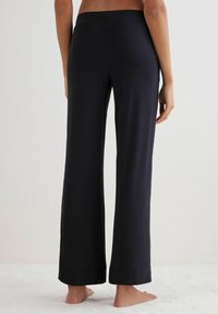 Pantalones de pierna ancha negros con una textura suave, cinturilla elástica y detalle de dobladillo plegado. La tela es ligera y se drapea cómodamente.