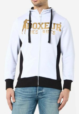 Ein Mann trägt einen weißen Kapuzenpullover mit Reißverschluss, schwarzen Bündchen und Saum, schwarzen Seitenpanelen sowie goldenem "Boxeur Des Rues"-Schriftzug mit Boxsilhouette auf der Brust.