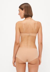 Beige bra with adjustable straps, smooth texture, and hook-and-eye closure. Paired with matching seamless boyshorts, also beige.