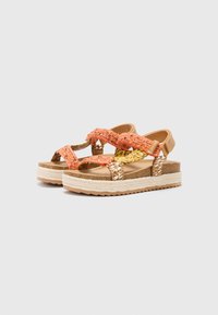 Sandales à brides avec un dessus tressé orange et jaune, une sangle de cheville beige et une semelle en liège épaisse et texturée avec des détails tressés blancs.