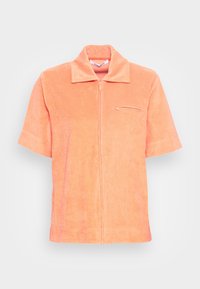 Chemise zippée à manches courtes en doux tissu éponge corail. Elle présente un col pointu et une petite poche sur le devant, à gauche de la poitrine.