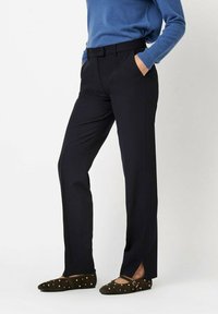 Black tailored trousers with a straight-leg design, featuring side pockets and a smooth fabric texture, paired with brown studded flats.