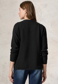 Schwarzer gerippter Pullover mit langen Ärmeln, rundem Ausschnitt und seitlichen Schlitzen, kombiniert mit blauen Jeans aus Denim, die einen strukturierten Stoff zeigen.