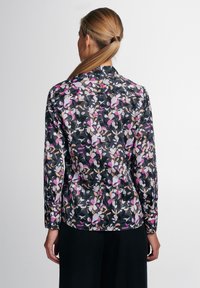 Camisa de manga larga con fondo negro, patrón floral en rosa, blanco y beige, con detalles de botones y un dobladillo redondeado.