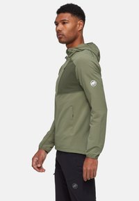 Lättviktsjacka i olivgrön färg med huva, med en strukturerad kropp och kontrasterande enfärgad panel, dragkedjefickor och logotyp på ärmen.