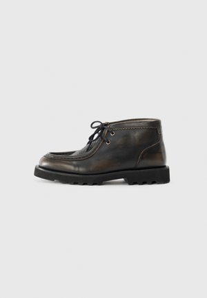 Botas de cuero marrón hasta el tobillo con puntera redondeada, cordones negros y un panel texturizado. Suela de goma negra resistente con detalle de tracción.