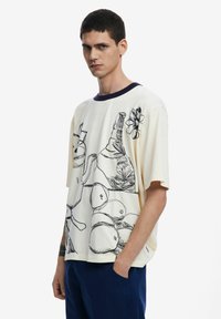 Short-sleeve cream t-shirt with navy collar featuring black line-art illustrations of various objects and flowers. Casual fit and fabric texture.
