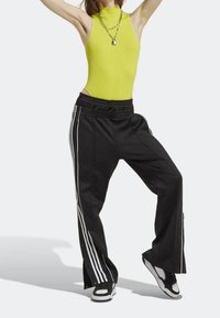 Neon gul ribbad bodysuit med hög krage, tillsammans med svarta vida byxor med vita sidostrimmor och elastisk midja.