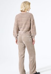 Beige gestreifter Pullover mit Ballonärmeln, kombiniert mit beigen Cordhosen. Weicher Stoff, lockere Passform und gerippte Bündchen sowie Bund.