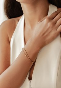 Pulsera de cadena de oro con un diseño minimalista que presenta una barra lisa y pequeños acentos esféricos, llevada en una muñeca desnuda.