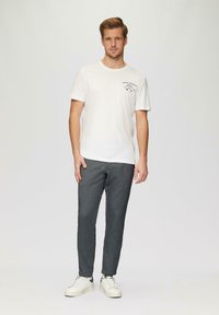 T-shirt en coton blanc avec un texte imprimé en marine et rouge, associée à un pantalon slim à motifs gris et à des baskets blanches.
