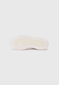 Semelle de sneaker rose clair en caoutchouc texturé, avec un motif en zigzag et une zone centrale lisse et légèrement surélevée pour l'adhérence.