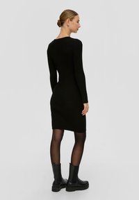 Schwarzes geripptes Strickkleid mit langen Ärmeln, taillierter Silhouette und runder Ausschnitt, kombiniert mit schwarzen Knöchelboots. Glatte Textur.