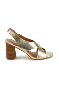 Gouden metalen slingback hoge hakken met een kruisbandontwerp, vierkante neus en een gestructureerde houten blokhak.