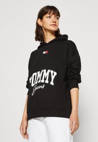 Felpa nera con testo bianco "TOMMY Jeans", caratterizzata da una piccola patch con logo in rosso, bianco e blu. Realizzata in tessuto morbido; vestibilità rilassata.