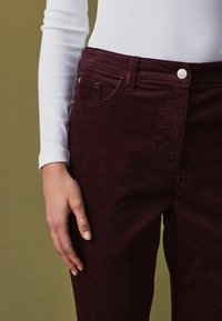 Bordeaux corduroy broek met een slim fit ontwerp, voorzien van een knoopsluiting aan de voorkant, zijzakken en een zachte verticale ribbelstructuur.