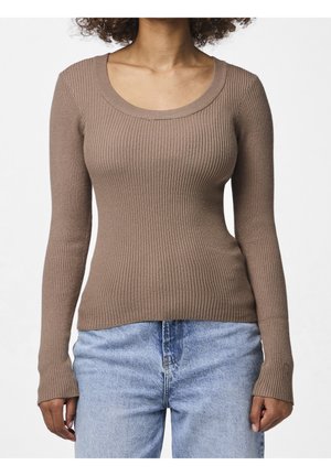 Femme portant un haut marron moulant à manches longues côtelées et un jean bleu clair taille haute sur un fond uni.