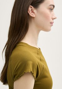Tricou scurt de culoare verde măslinie, cu mâneci scurte și guler rotund, având detalii de cusătură subtile pe material.