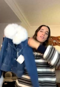 Personne portant un pull rayé tenant une veste en jean bleue avec un col blanc et douillet en intérieur.