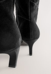 Schwarze Wildleder-Stiefel mit Absatz, spitzer Zehenpartie und 7,5 cm Absatzhöhe. Verfügt über einen Seitenschlitz und eine strukturierte Oberfläche für besseren Halt.