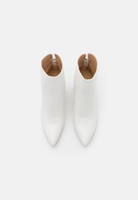 Białe botki za kostkę z ostrym nosem i gładką teksturą. Mają krótki mankiet oraz subtelny zamek błyskawiczny z tyłu.