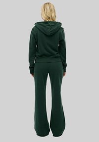 Sweatshirt à capuche vert foncé et pantalon évasé assorti en tissu doux, avec un design simple et une coupe décontractée.
