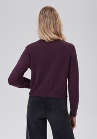 Violetinis švarkelis su apvaliu kaklu ir ilgomis rankovėmis, turintis trumpą dizainą. Derinamas su tamsiomis, aukštu liemeniu džinsais.