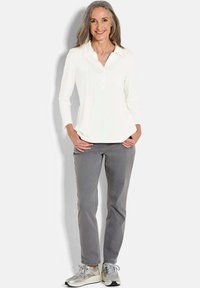 Camicetta bianca a maniche lunghe con placca dei bottoni e dettagli a pieghe, abbinata a pantaloni grigi a gamba dritta e sneakers argentate.